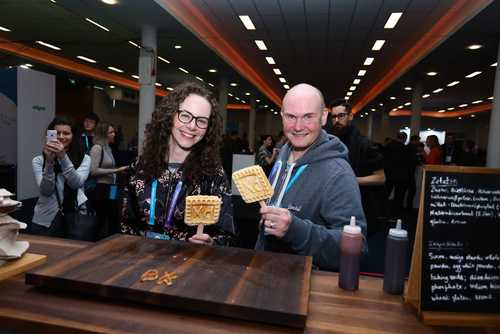 A woman and a man smiling holding up their waffles.