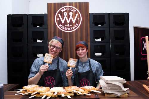 A man and a woman smiling holding up waffles at the Adobe stand.