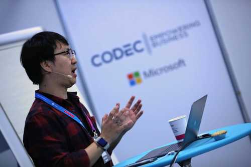 A man speaking on stage with a Microsoft logo in the background.